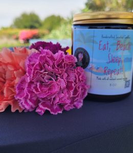 Handcrafted House of Mosaic candle displayed with pink flowers at an outdoor pop-up market.